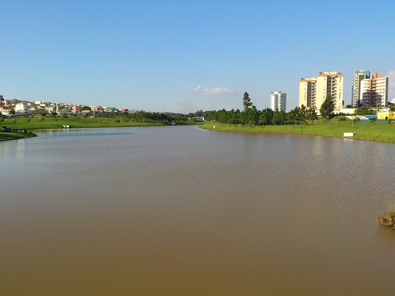 Lago do Parque Ecológico de Indaiatuba, São Paulo, com gramado nas margens e prédios residenciais ao fundo
